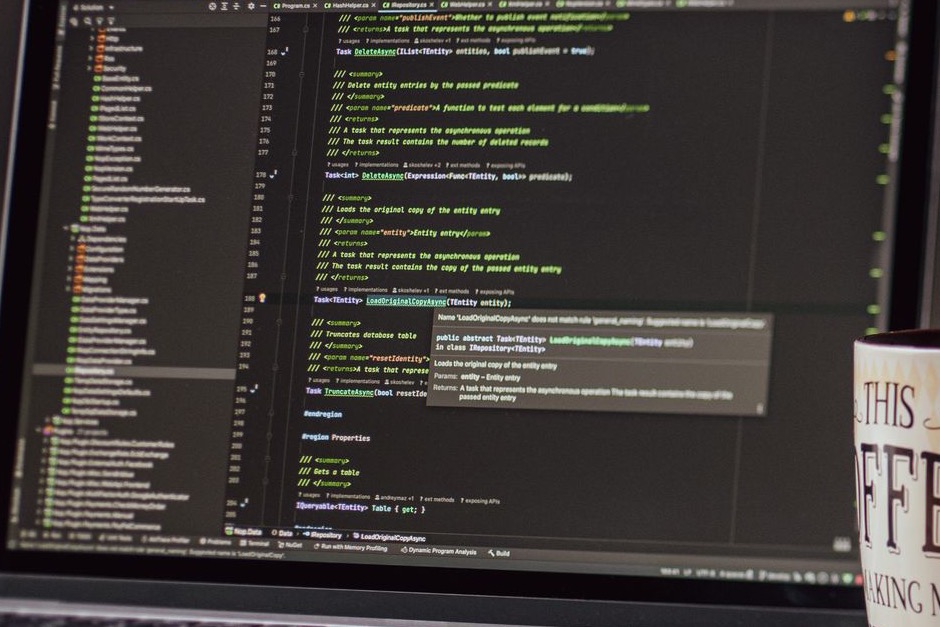 A laptop on a desk displaying a code editor next to a coffee mug