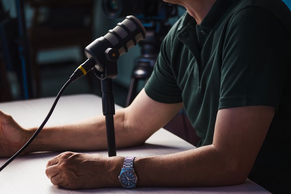 A person seated at a table speaking into a studio microphone while recording a podcast