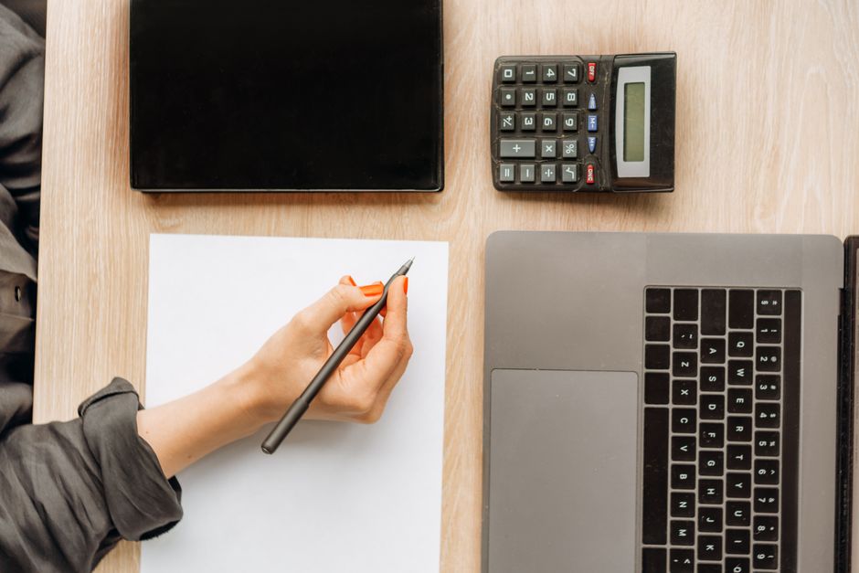 Overhead view of a desk with a laptop, calculator and notepad, comparing costs